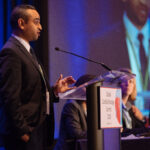 A man standing a podium giving a presentation on cardio-oncology research