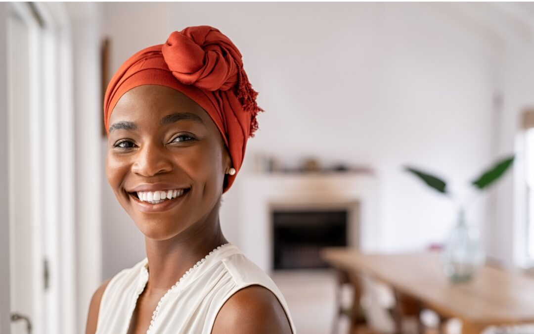 A black woman wearing a orange head covering, smiling