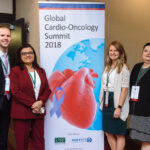 2018 Cardio Oncology Summit MORNING SESSION-83 A man and three women pose in front of a banner for the Global Cardio-Oncology Summit in 2018