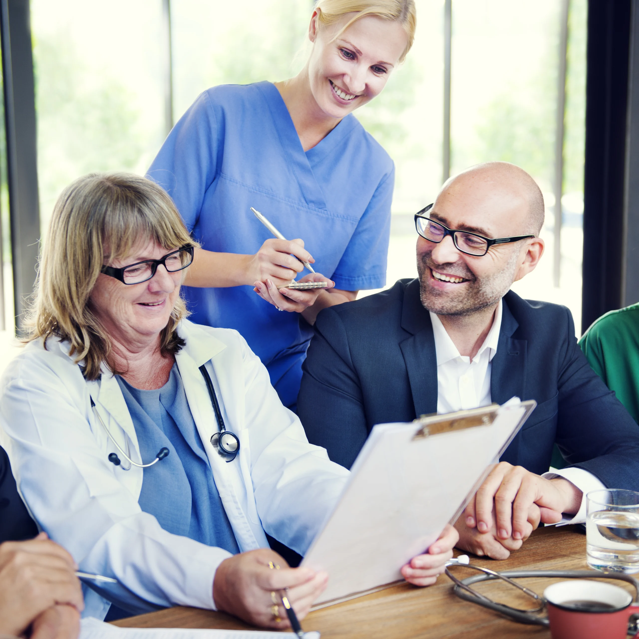 A doctor, businessman, and nurse smile while reviewing a document.