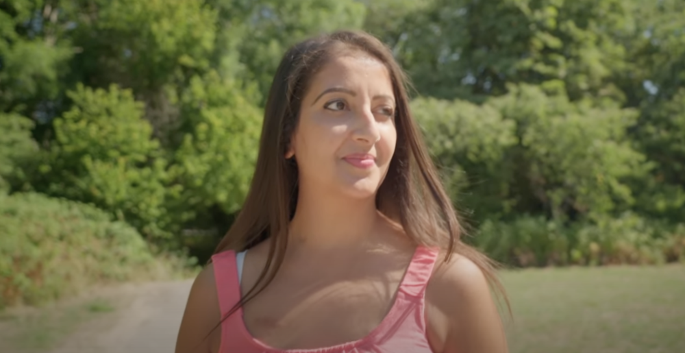 Kreena walks in front of a wooded path