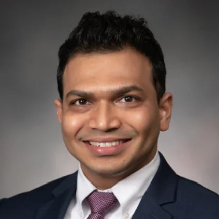 Amit Arbune, MD, MHA, FACC, an Indian cardiologist wearing a dark suit against a gradient background